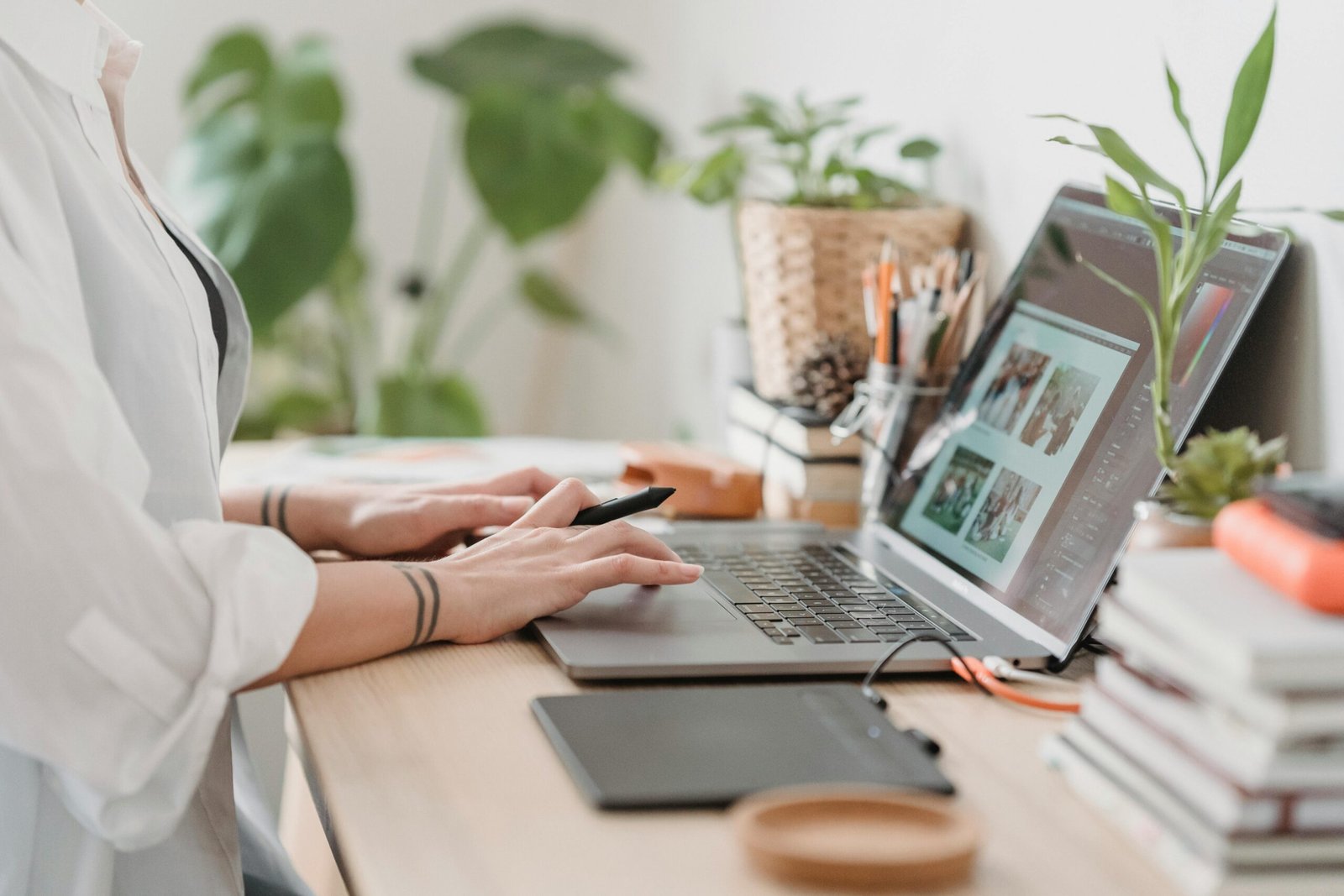 Freelance designer working from home using a laptop and digital tablet, surrounded by plants.